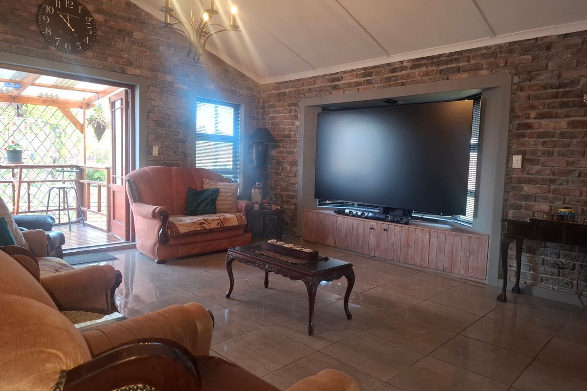 Spacious living room featuring exposed brick walls, vaulted ceilings, tiled flooring, and a built-in media cabinet with direct access to an outdoor patio area.