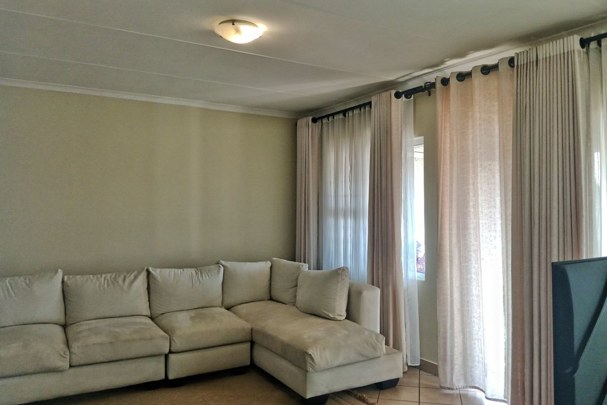 A living room featuring tiled flooring, neutral wall tones, and floor-to-ceiling curtains providing access to an outdoor area.