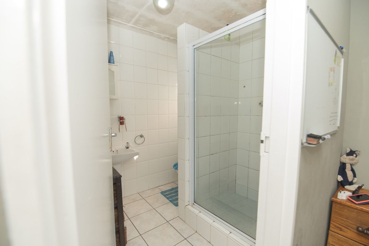 A functional bathroom featuring a walk-in shower with glass enclosure, wall-mounted basin, and tiled flooring.