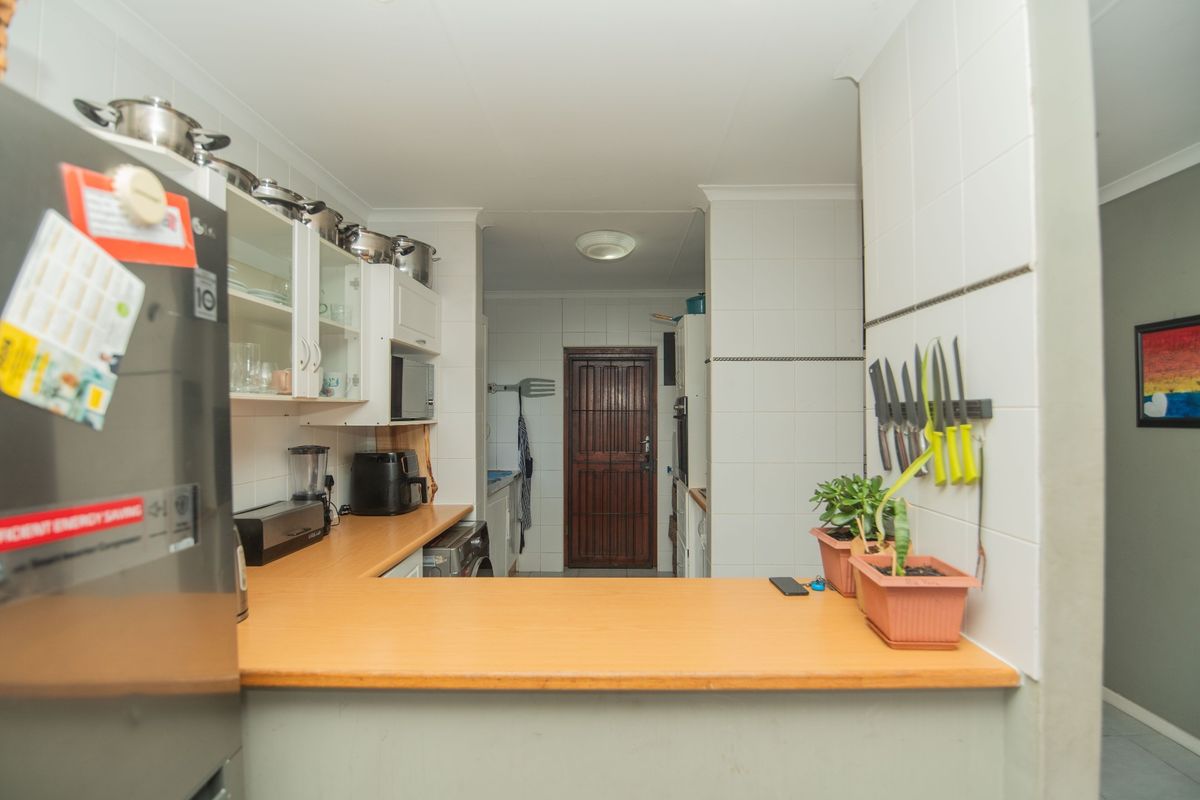 A functional kitchen featuring laminate countertops, white cabinetry, tiled walls, and a breakfast bar, leading to a rear access door.