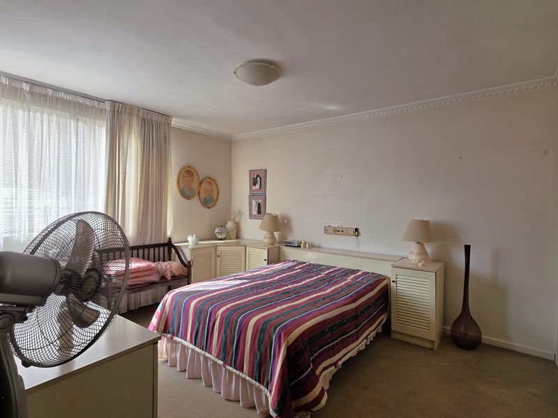 A bedroom featuring built-in cabinetry and headboard, carpeted flooring, and decorative ceiling cornicing, offering a functional layout with potential for modernization.