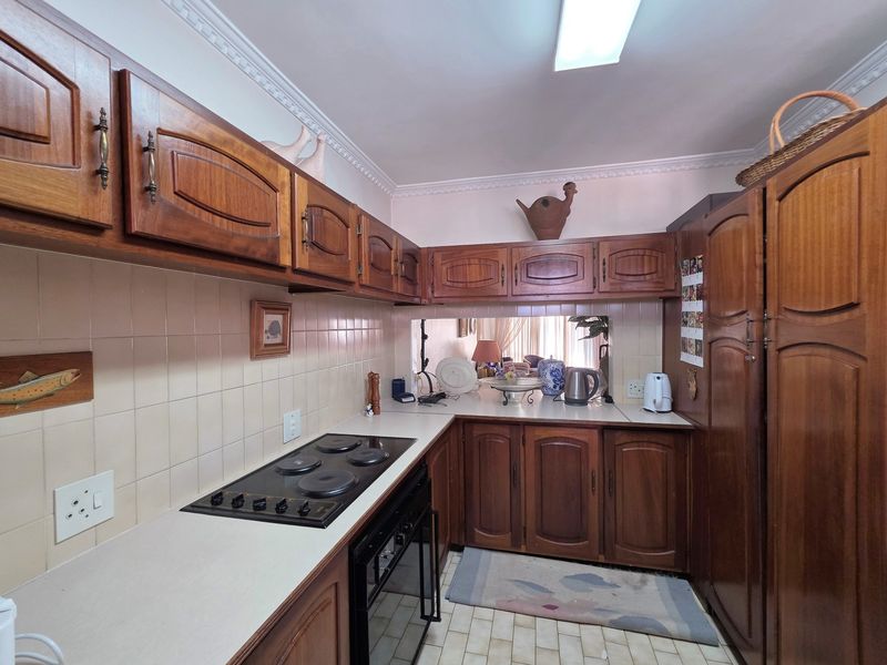 A functional kitchen featuring traditional wooden cabinetry, an integrated electric hob and oven, tiled backsplash, and durable tiled flooring.