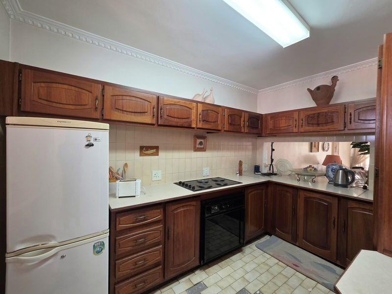 A functional kitchen featuring traditional wooden cabinetry, laminate countertops, built-in oven, electric hob, and tiled backsplash with a pass-through window to the living area.
