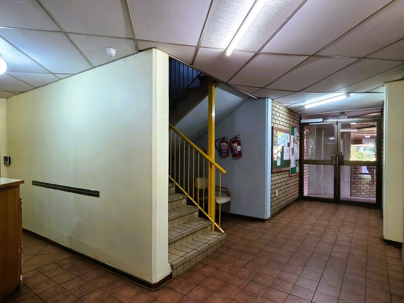 A communal apartment building entrance lobby featuring tiled flooring, a staircase with metal balustrade, and a glass entrance door.