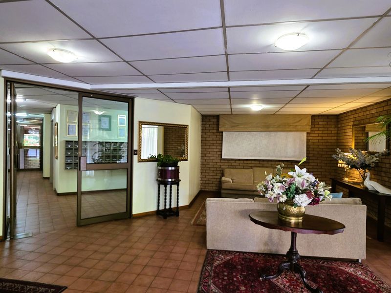 A spacious apartment building entrance lobby featuring tiled flooring, exposed brick walls, and a drop ceiling with integrated mailboxes.