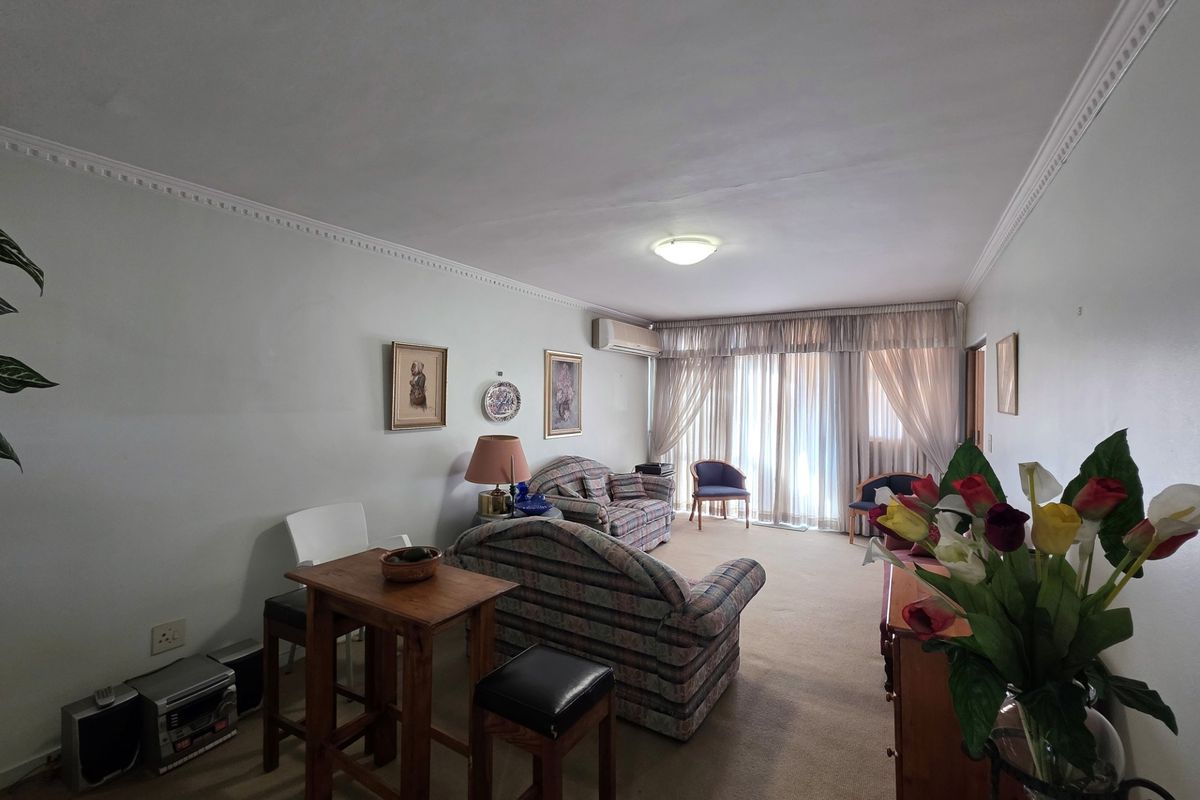 A living room featuring carpet flooring, ceiling cornices, and sliding glass doors leading to an outdoor area, equipped with a wall-mounted air conditioning unit.