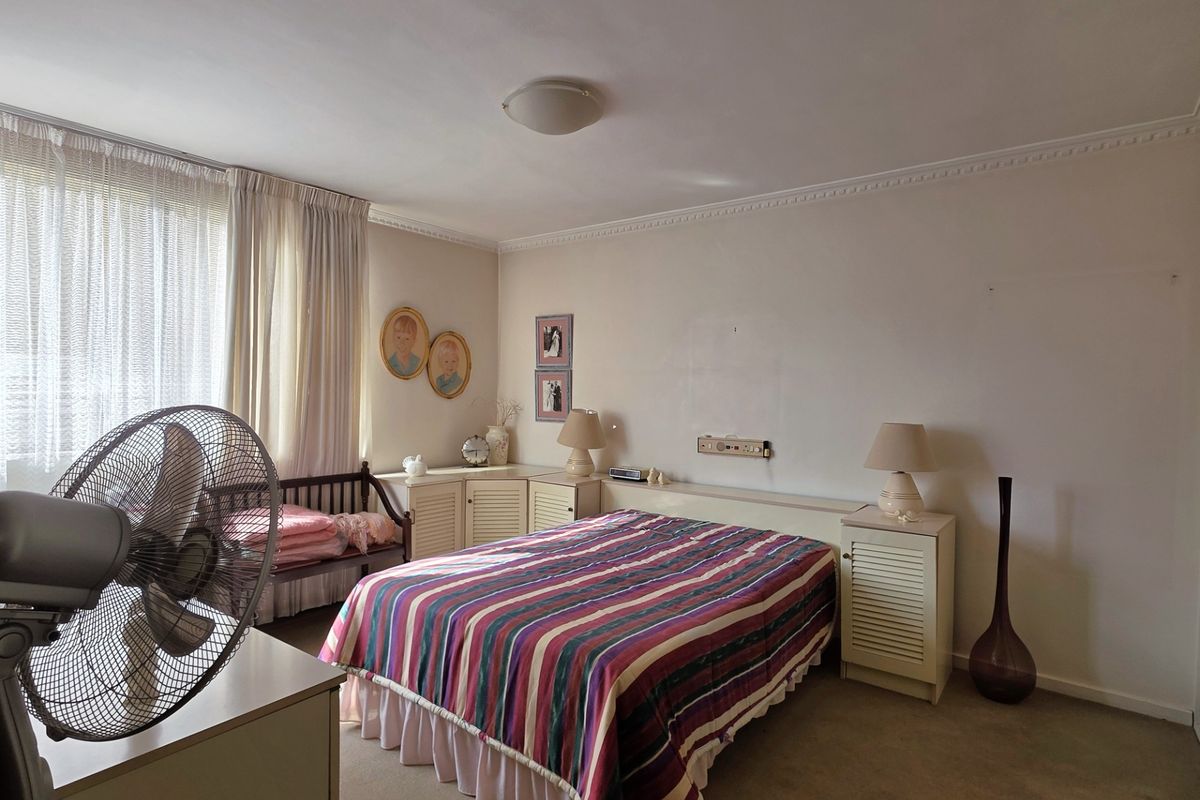 A bedroom featuring built-in cabinetry and headboard, carpeted flooring, and decorative ceiling cornicing, offering a functional layout with potential for modernization.