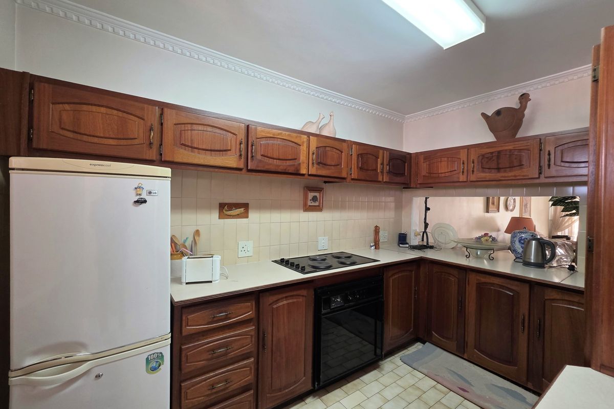 A functional kitchen featuring traditional wooden cabinetry, laminate countertops, built-in oven, electric hob, and tiled backsplash with a pass-through window to the living area.