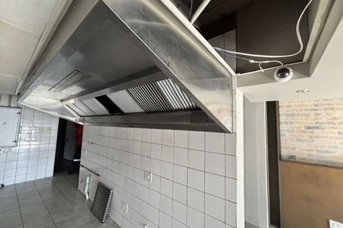 Commercial kitchen area featuring a large stainless steel extractor hood, tiled walls, and tiled flooring, currently requiring maintenance and ceiling repairs.