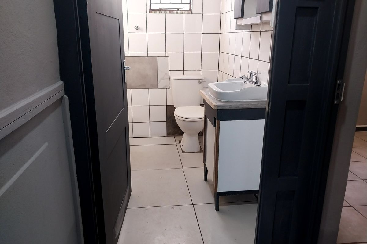 A functional bathroom featuring a white ceramic toilet, a vanity basin, and tiled walls and flooring.