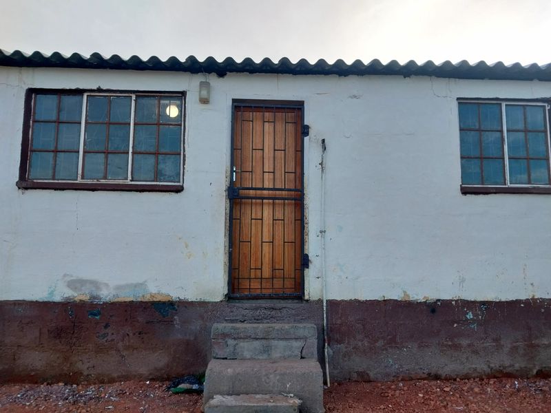Exterior view of a residential building featuring a wooden door with security gate, two windows, and concrete steps leading to the entrance.