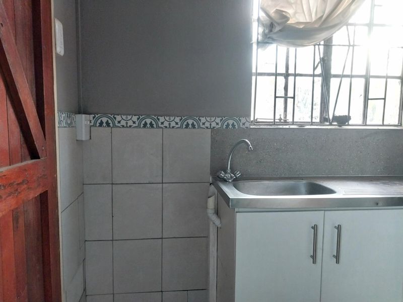 A functional laundry area featuring a stainless steel sink, built-in base cabinetry, and tiled splashback with decorative border detailing.