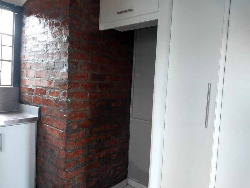 A kitchen area featuring a combination of modern white cabinetry and a rustic exposed brick feature wall with a stainless steel sink.