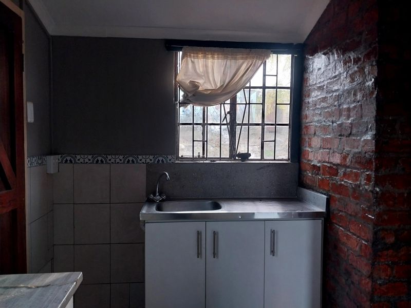 A functional scullery area featuring a stainless steel sink, built-in cabinetry, tiled splashback, and an exposed brick feature wall.