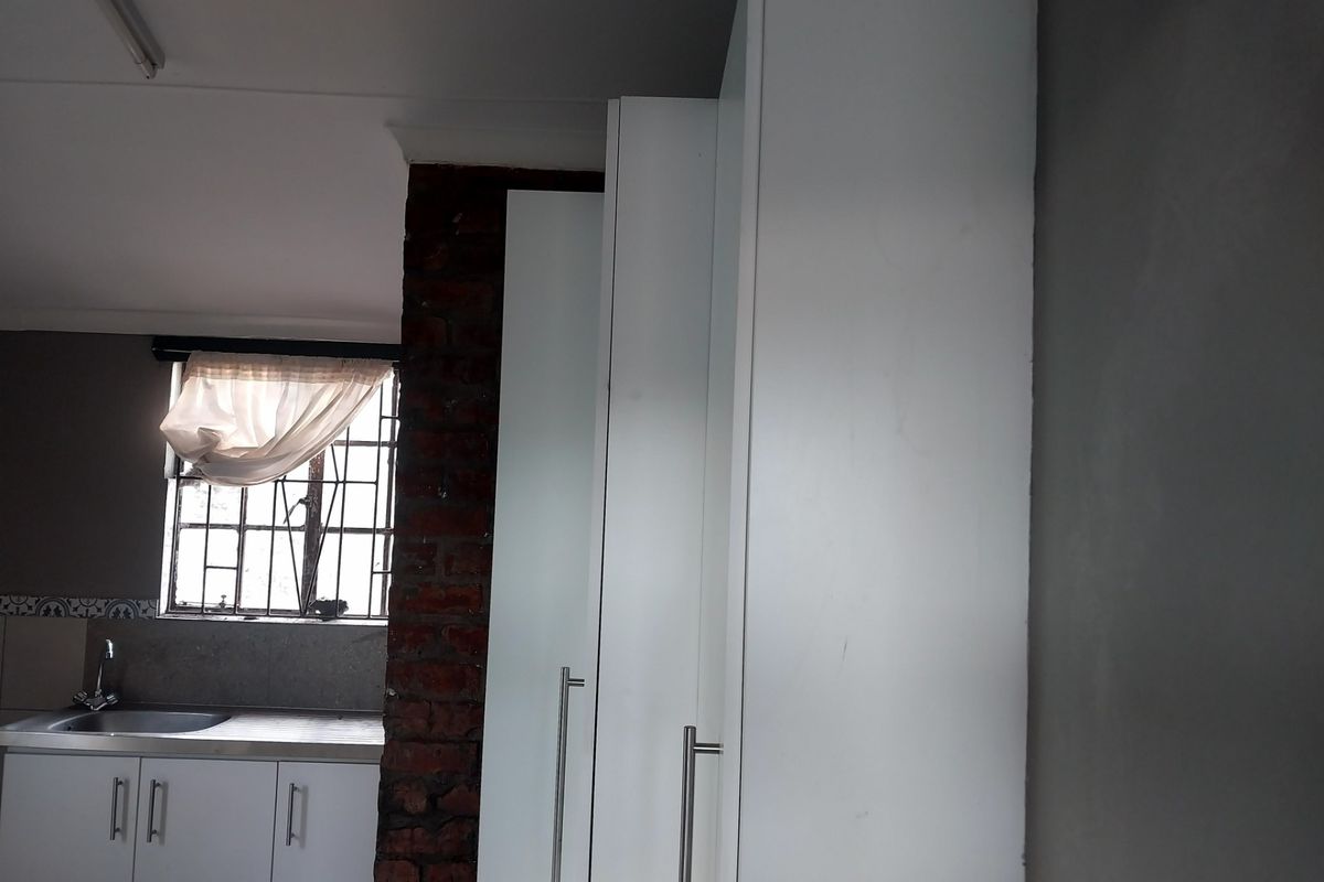 A kitchen area featuring white cabinetry, a stainless steel sink, and a window with security bars, accented by an exposed brick pillar.