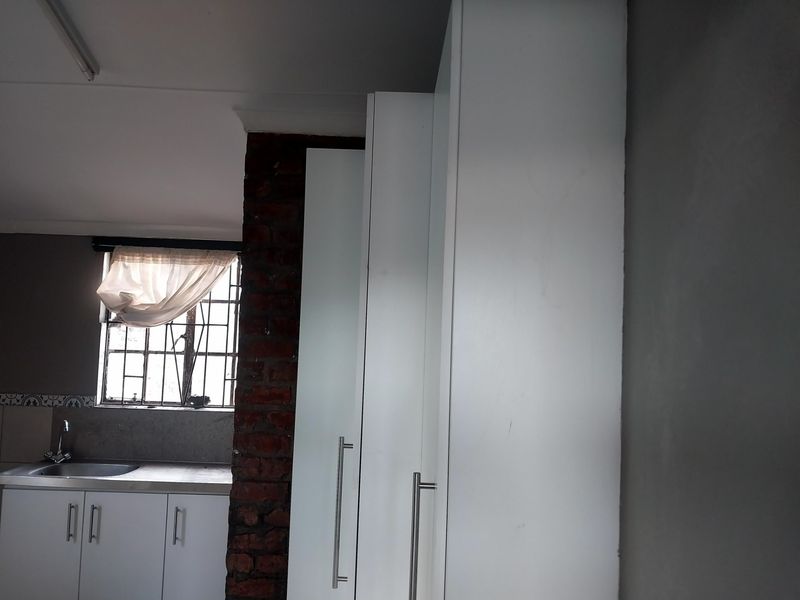 A kitchen area featuring white cabinetry, a stainless steel sink, and a window with security bars, accented by an exposed brick pillar.