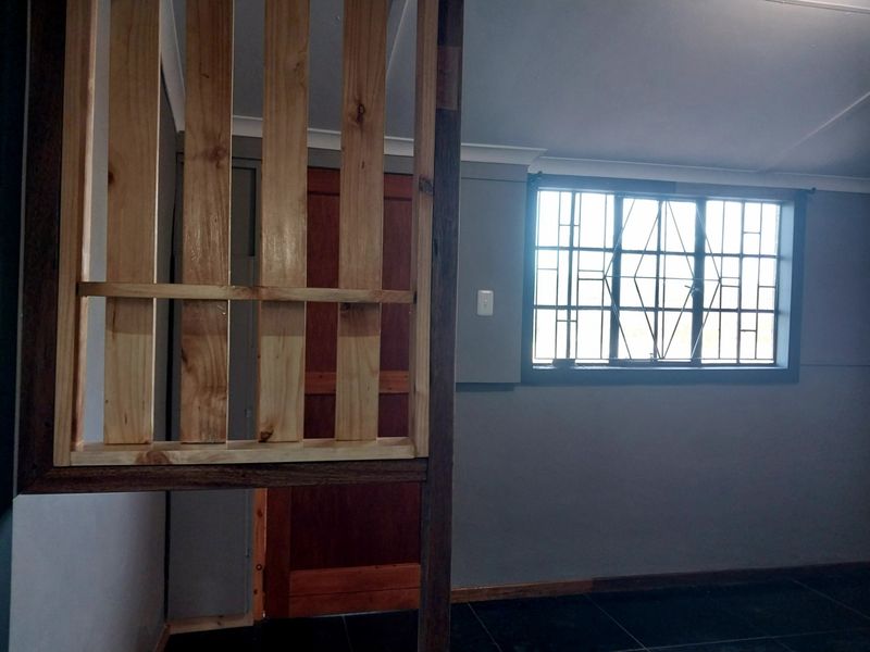 A bedroom interior featuring dark floor tiles, a wooden room divider, and a window fitted with security burglar bars.