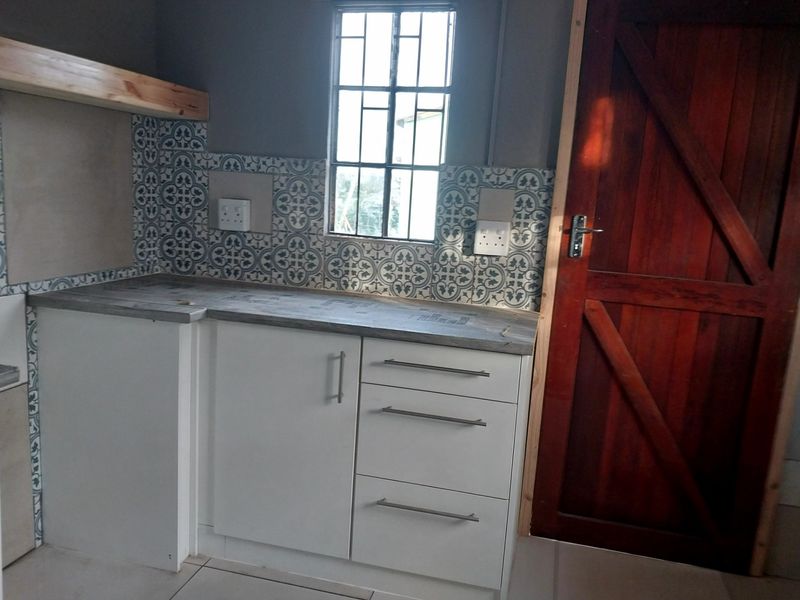A compact kitchen area featuring modern white cabinetry, patterned tile splashbacks, a wooden countertop, and a rustic timber door.