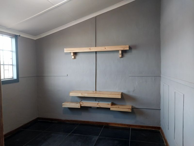 A vacant room featuring dark floor tiles, grey painted walls with paneling detail, and custom-mounted timber shelving units.