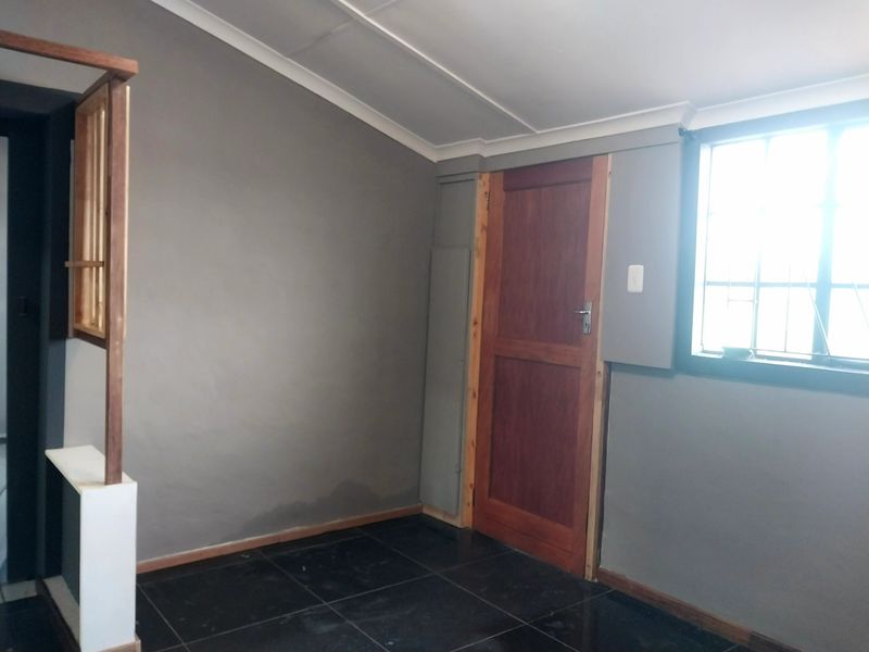 An interior room featuring dark tiled flooring, grey painted walls, and a wooden door, showing signs of moisture damage on the lower wall section.