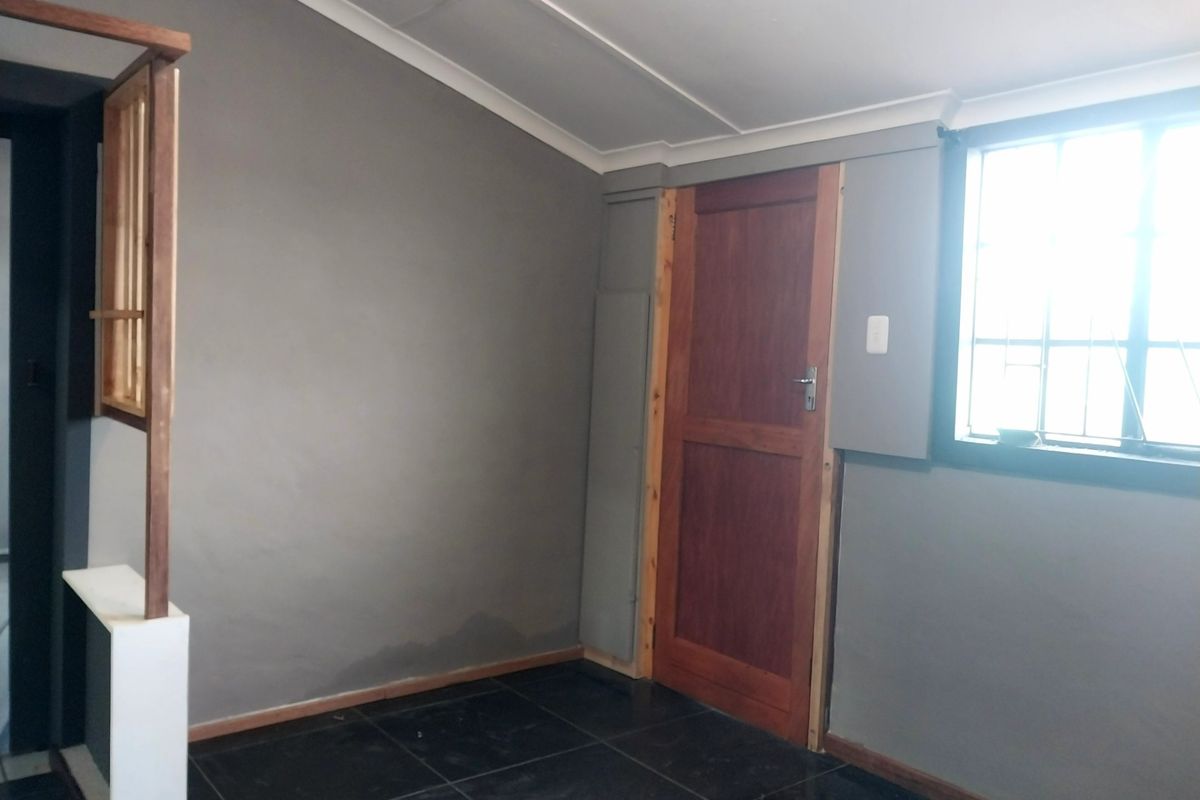An interior room featuring dark tiled flooring, grey painted walls, and a wooden door, showing signs of moisture damage on the lower wall section.