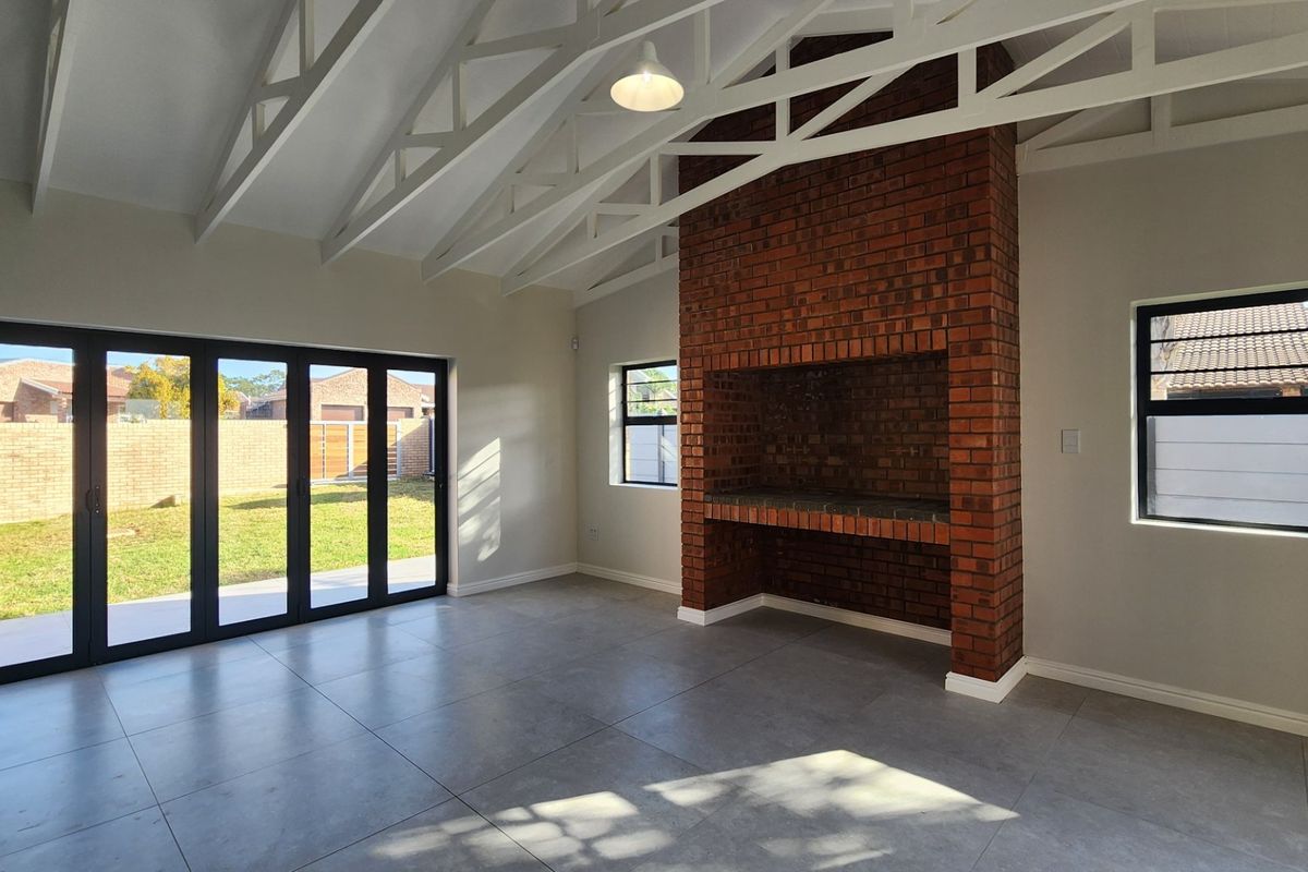 Spacious living area featuring a vaulted ceiling with exposed trusses, large brick fireplace, tiled flooring, and folding glass doors opening to the rear garden.