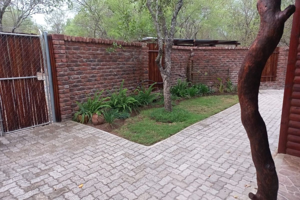 A private rear courtyard featuring a paved surface, brick boundary walls, and a small landscaped garden area with established trees.