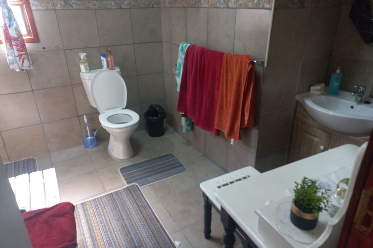 A functional bathroom featuring full-height ceramic wall tiling, a standard toilet, and a vanity unit with an integrated washbasin.