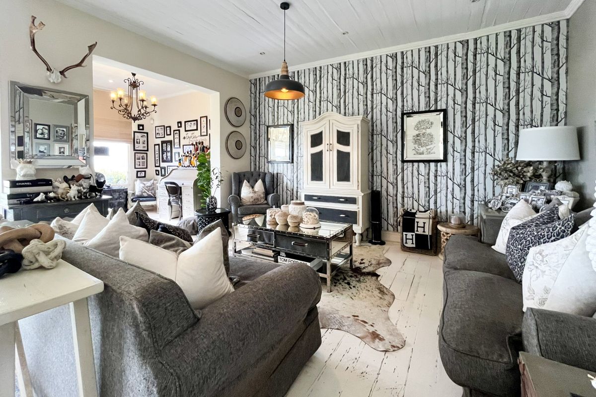 A cozy living room featuring a distinctive forest-themed wallpaper accent wall, painted timber flooring, and a white timber plank ceiling with pendant lighting.