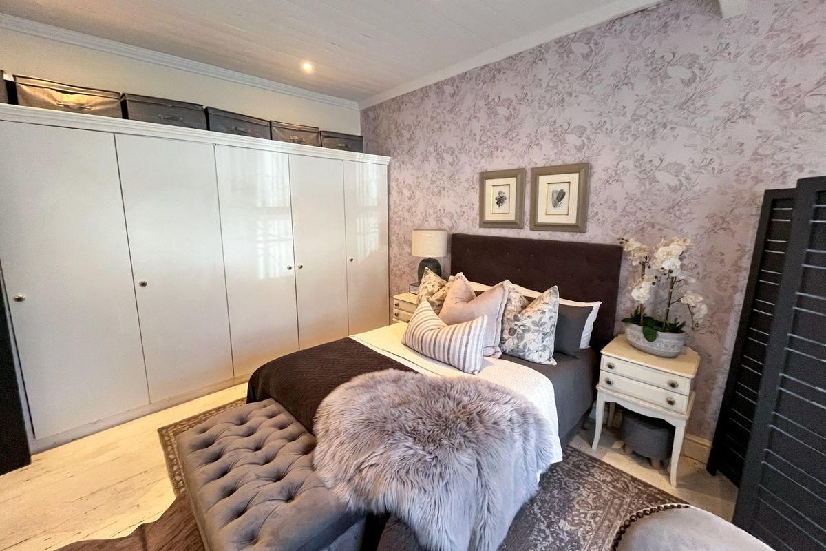 A well-maintained bedroom featuring a large built-in wardrobe, decorative wallpaper, and recessed downlighting set into a timber ceiling.