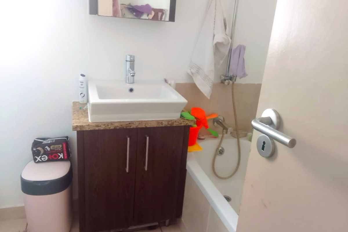 A compact bathroom featuring a vanity with a stone-look countertop, a vessel sink, and a combined shower and bathtub unit.