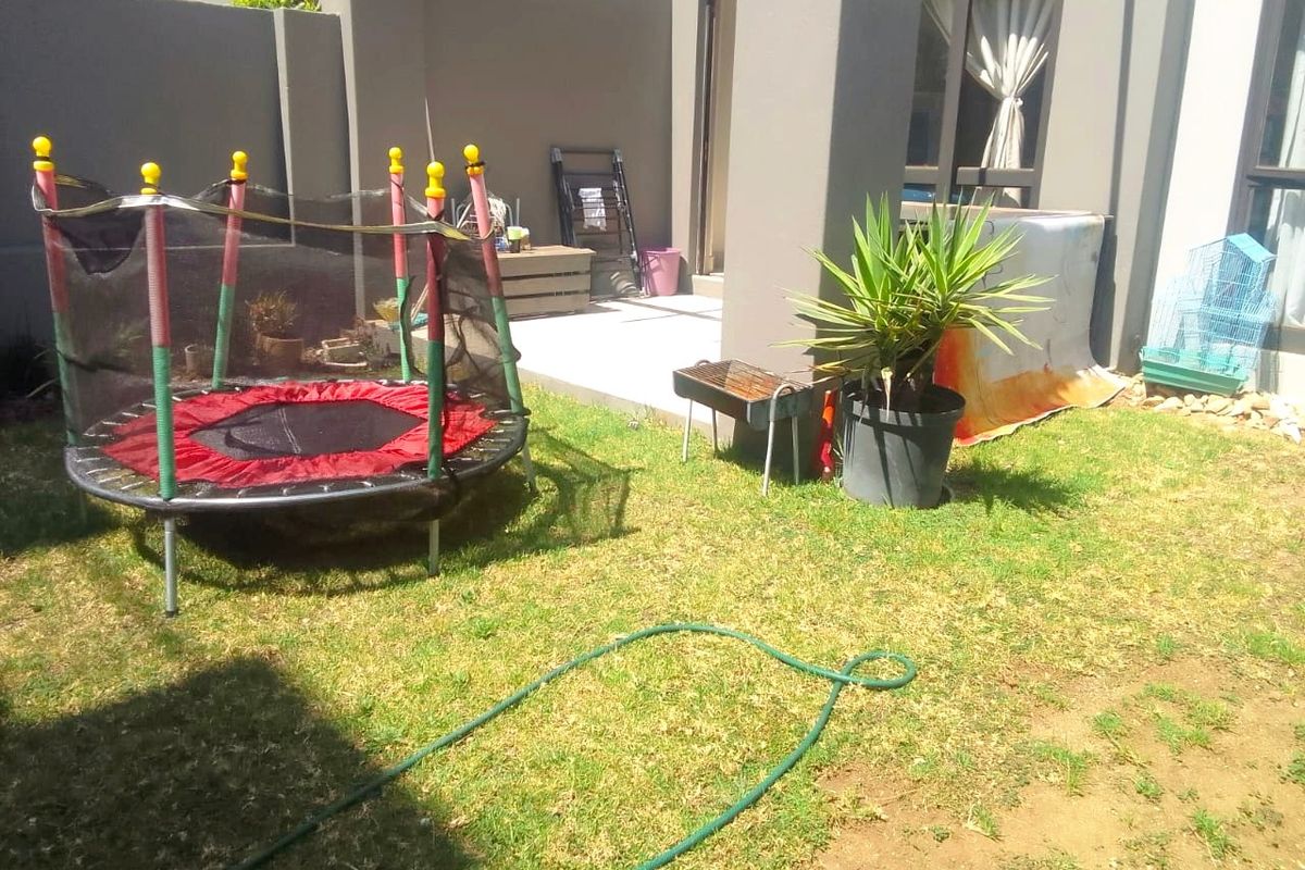 A private rear garden area featuring a paved patio section and a small lawn, directly accessible from the apartment living space.
