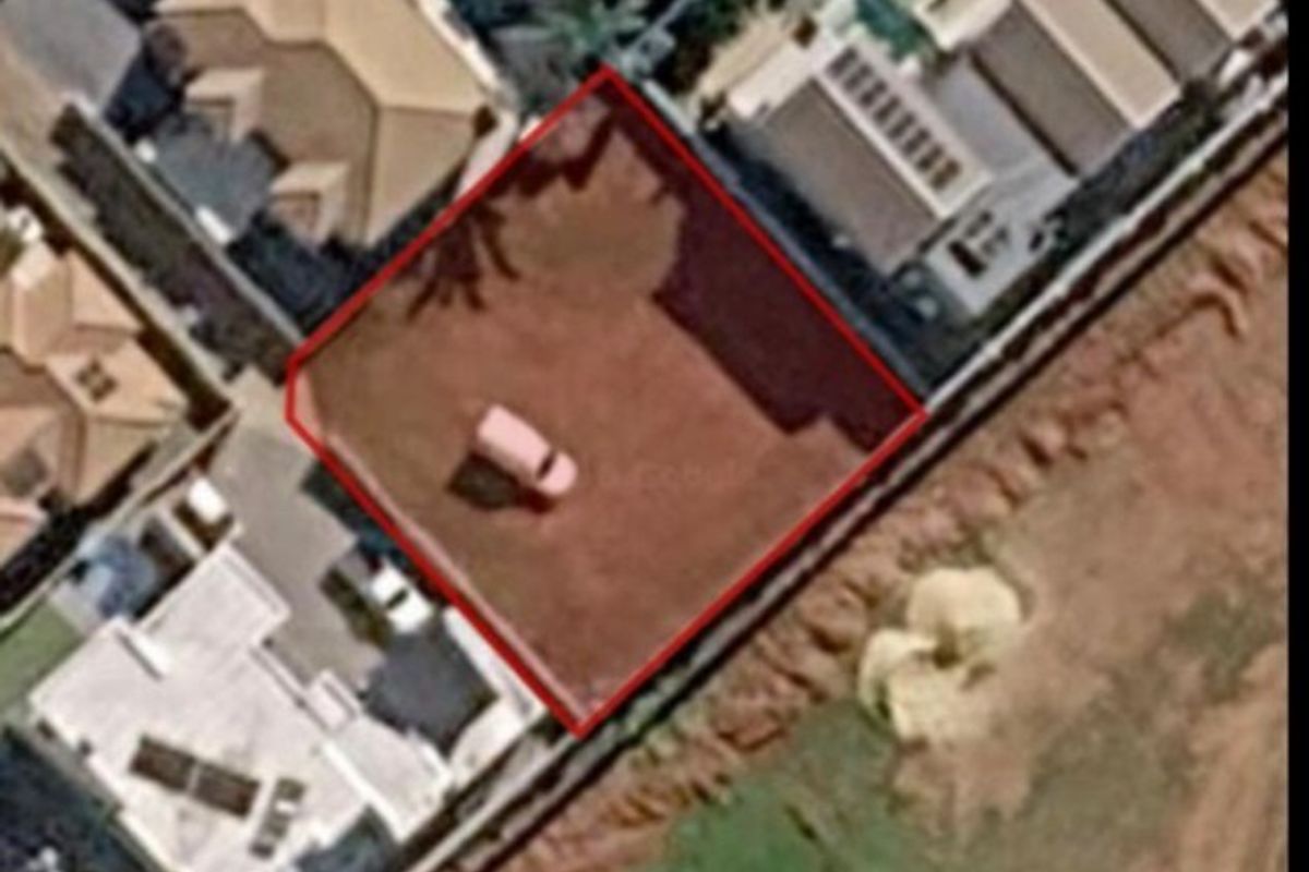 An aerial view of a vacant residential plot of land, clearly outlined in red, situated within an established neighborhood.