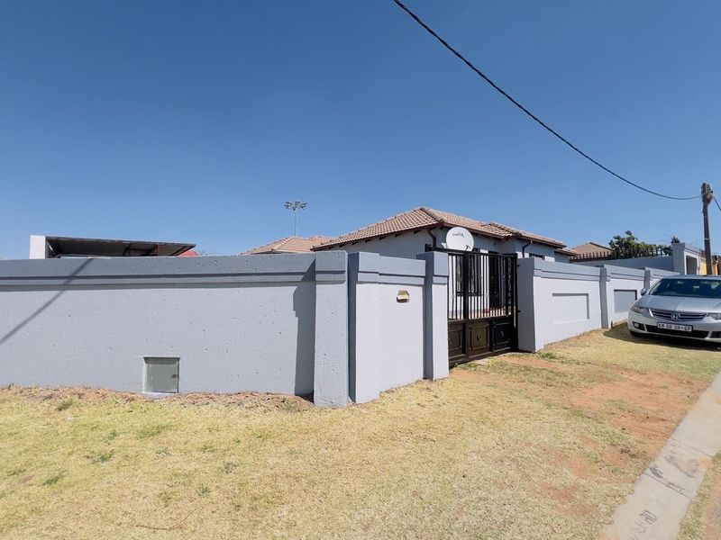 Front view of the property featuring a secure perimeter wall, metal entrance gate, and tiled roof structure.