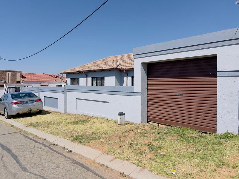 Front exterior view of the property featuring a secure perimeter wall, tiled roof, and a brown roller garage door.