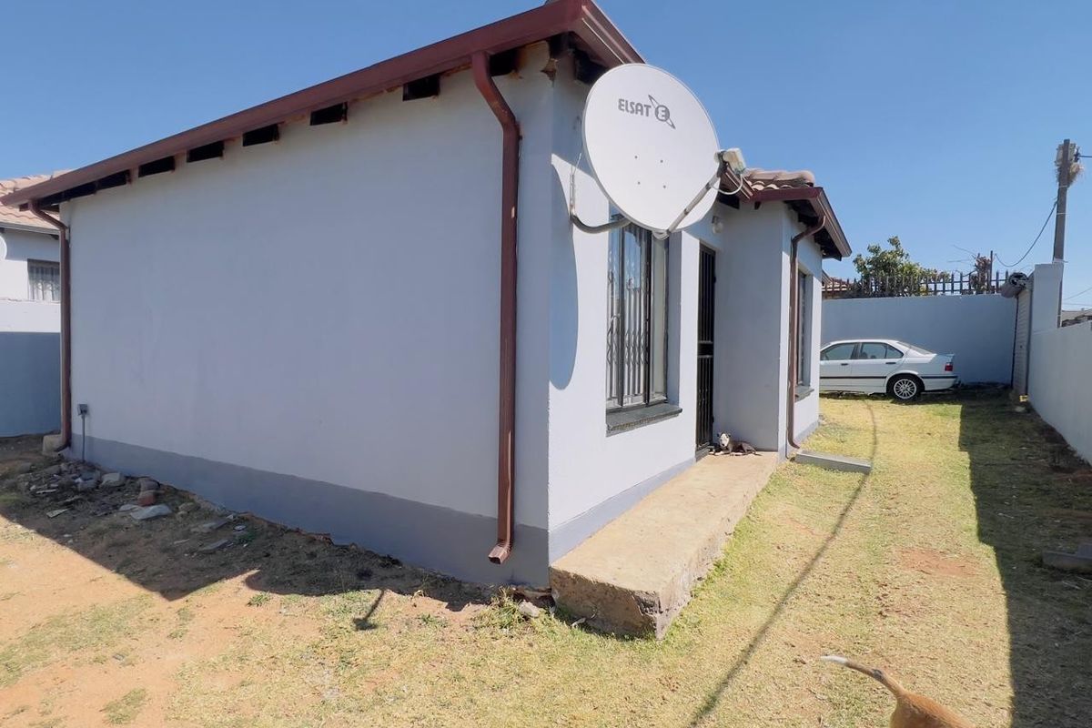 Rear view of the property showing the exterior wall, satellite dish, and concrete entrance step with security bars on the windows.