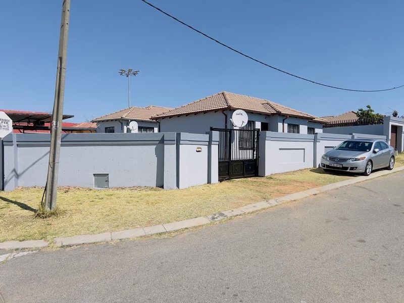 Front view of a residential property featuring a secure perimeter wall, metal gate, and tiled roof structure.