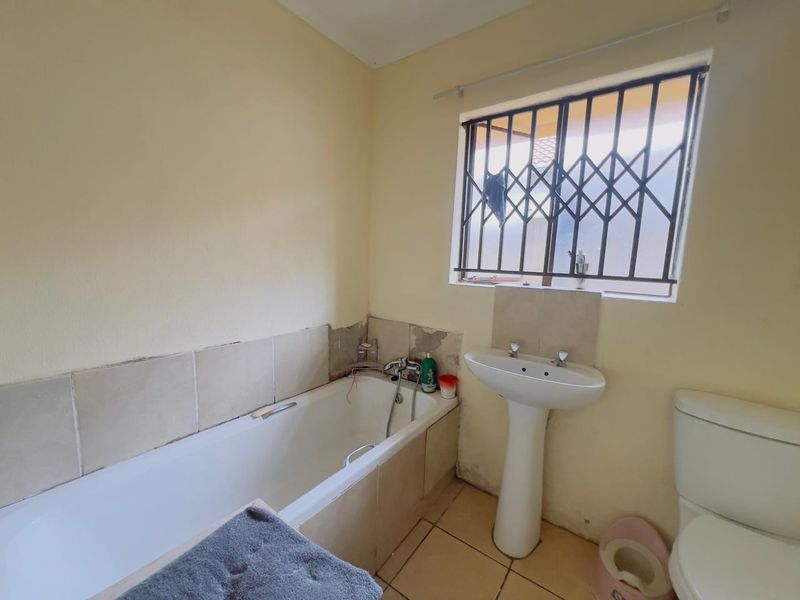 A functional bathroom featuring a bathtub, pedestal basin, and toilet, requiring cosmetic updates and tile repairs to restore its condition.