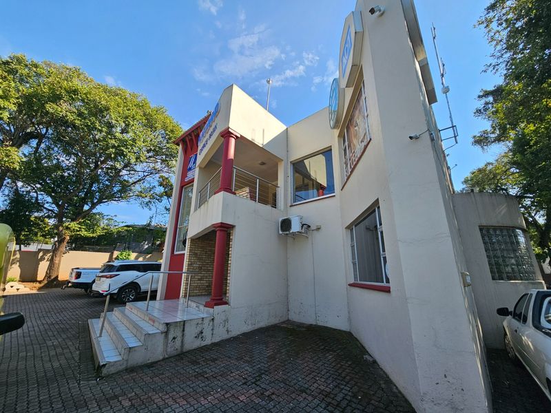 Exterior view of a multi-level office building featuring a covered entrance, balcony, and paved parking area.