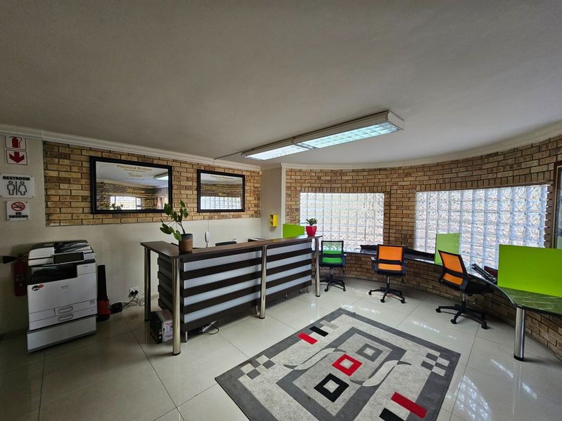 A functional office reception area featuring exposed brick walls, glass block windows, tiled flooring, and a built-in reception desk.