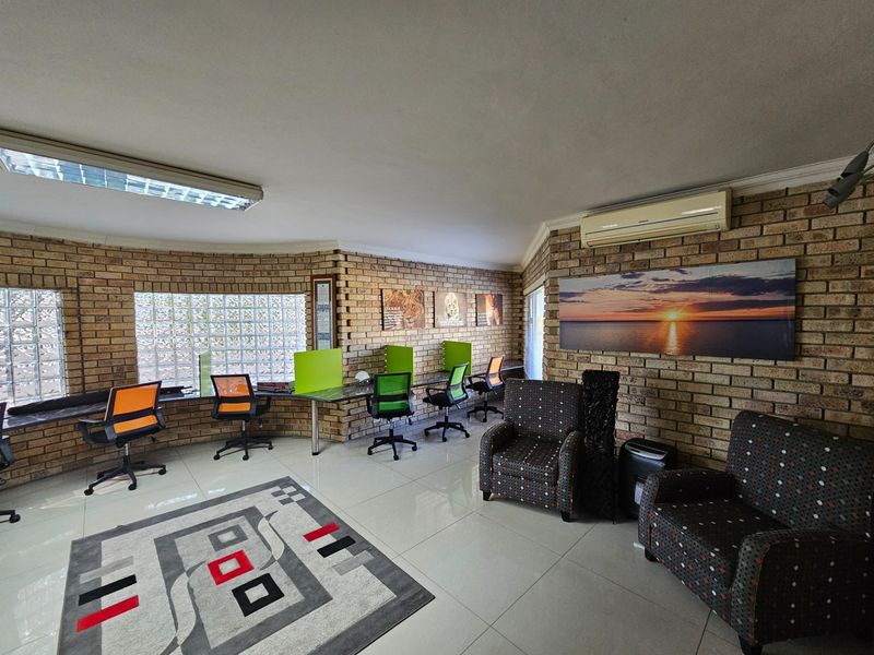 A spacious office area featuring exposed brick walls, tiled flooring, glass block windows, and a wall-mounted air conditioning unit.
