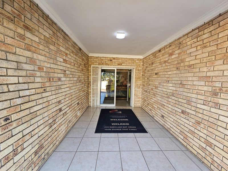 A covered entrance area featuring face brick walls, tiled flooring, and a glass door leading into the office space.