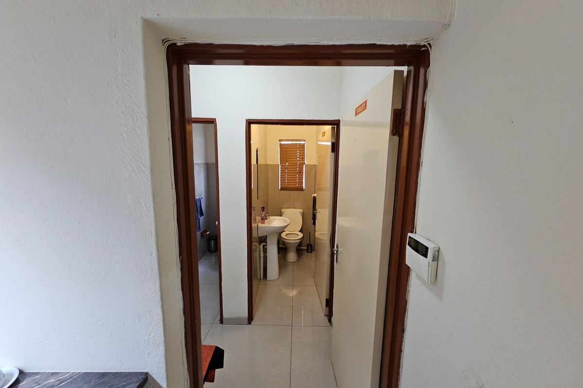 A view through a doorway into a functional office bathroom featuring a pedestal basin, toilet, and tiled flooring.