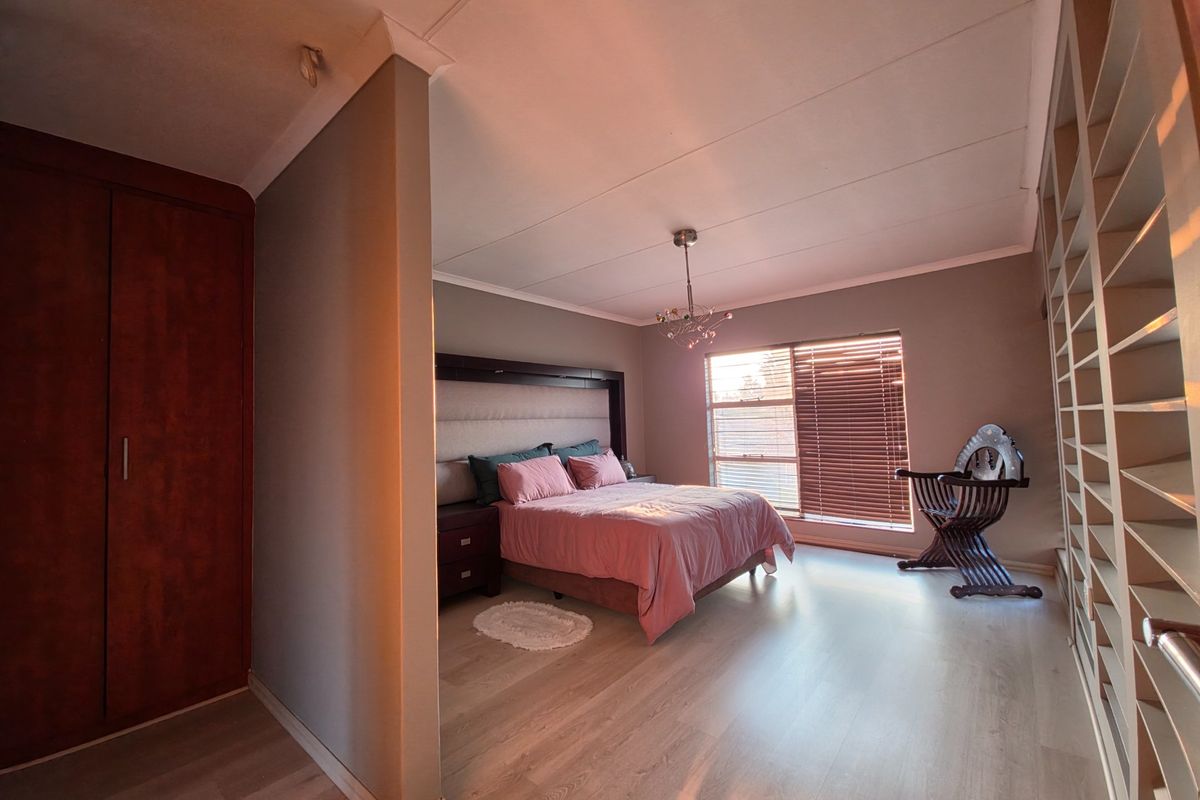 Spacious bedroom featuring light laminate flooring, extensive built-in storage, and large windows with venetian blinds, creating a bright and functional living space.