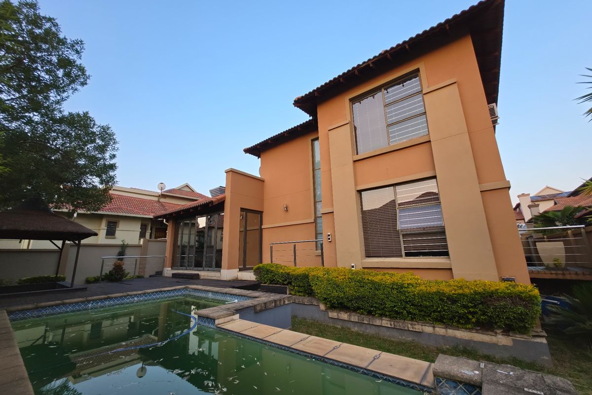 Rear exterior view of a two-storey house featuring a swimming pool, timber decking, and established garden hedging.