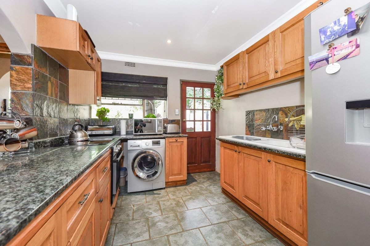 A functional kitchen featuring wooden cabinetry, granite countertops, slate tile backsplash, and integrated appliances with direct access to the exterior.