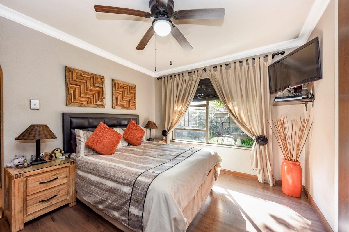 A well-maintained bedroom featuring laminate flooring, a ceiling fan, and a window with security bars, offering a comfortable and functional living space.