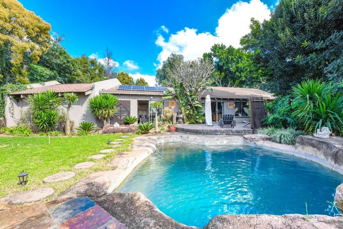 Rear view of the property featuring a landscaped garden, a natural-style swimming pool, a paved patio area, and roof-mounted solar panels.