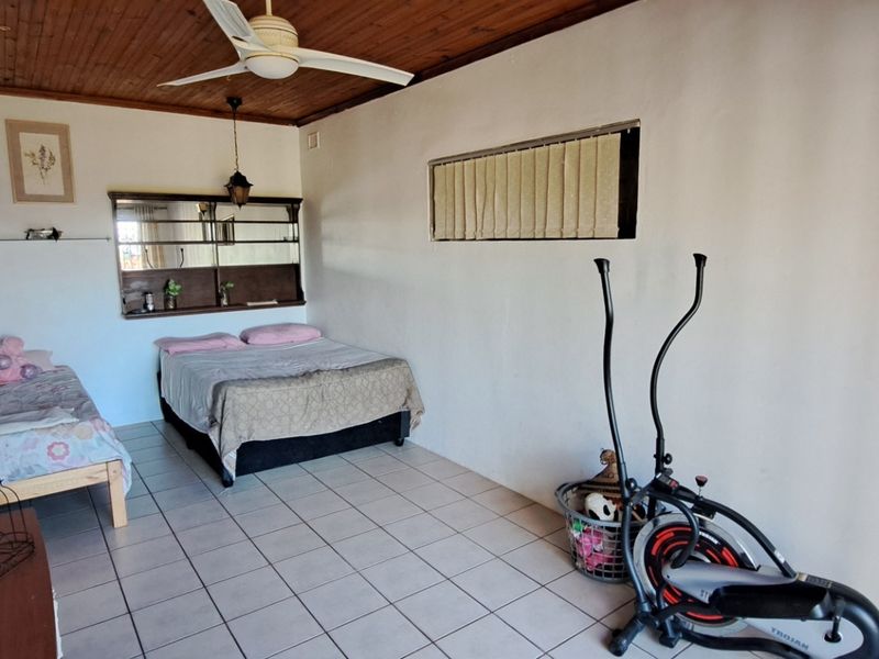 Spacious bedroom featuring tiled flooring, a timber-paneled ceiling with a fan, and a built-in wall mirror unit.