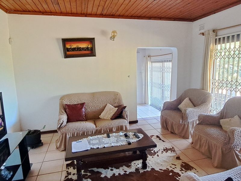 A living room featuring a timber-clad ceiling, ceramic tiled flooring, and a sliding glass door with a security gate leading to the exterior.